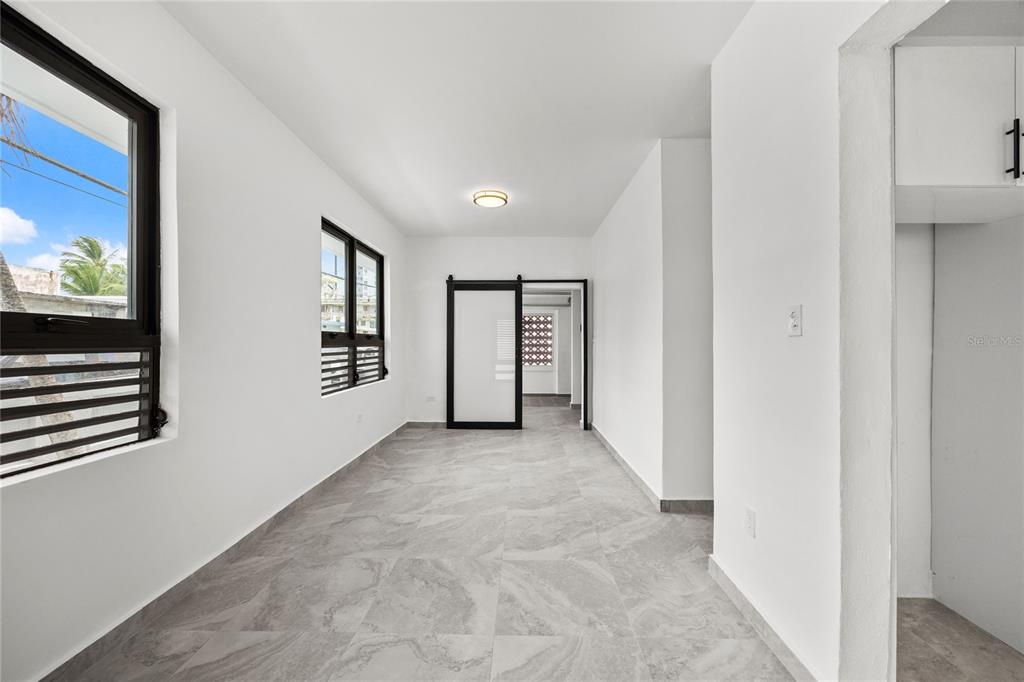 A bright, empty room features white walls, gray tile flooring, and a black sliding door — 107 ESPERANZA, LUQUILLO, PR