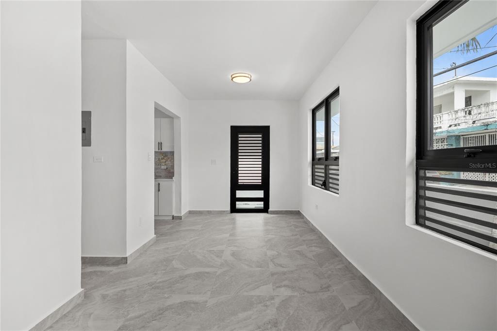 A bright, empty room features white walls, gray tiled flooring, and a black-framed door — 107 ESPERANZA, LUQUILLO, PR