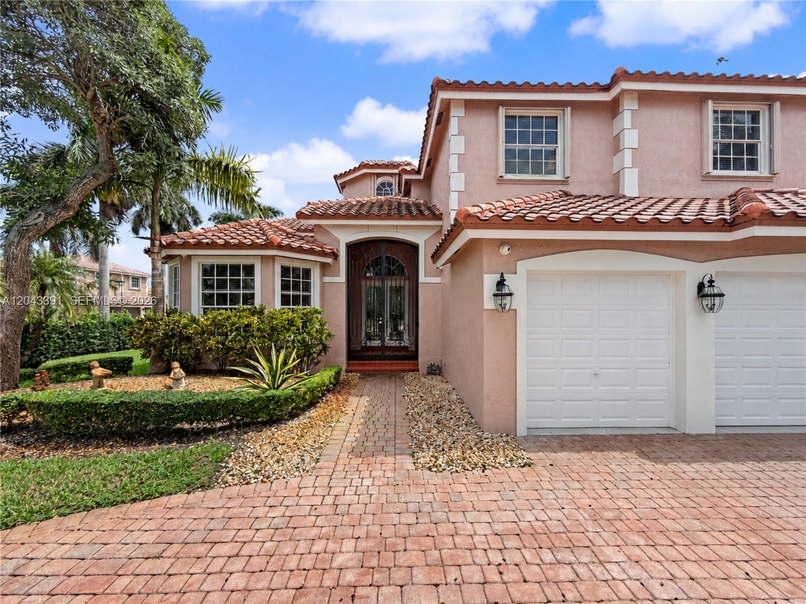 A two-story pink stucco house features a tiled roof, brick driveway, and arched entryway — 18900 SW 32nd Ct, Miramar FL 33029, MIRAMAR, FL
