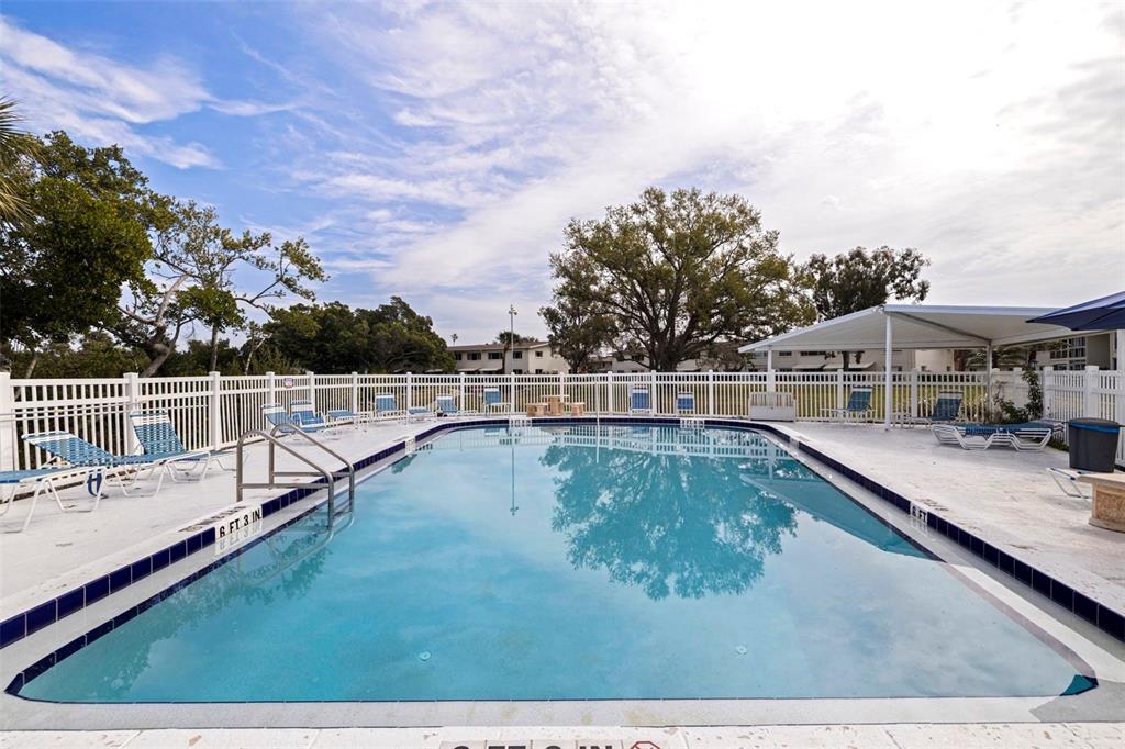 An outdoor swimming pool is surrounded by a white fence, lounge chairs, and trees — 4480 OVERLOOK DRIVE NE UNIT 12, ST PETERSBURG, FL