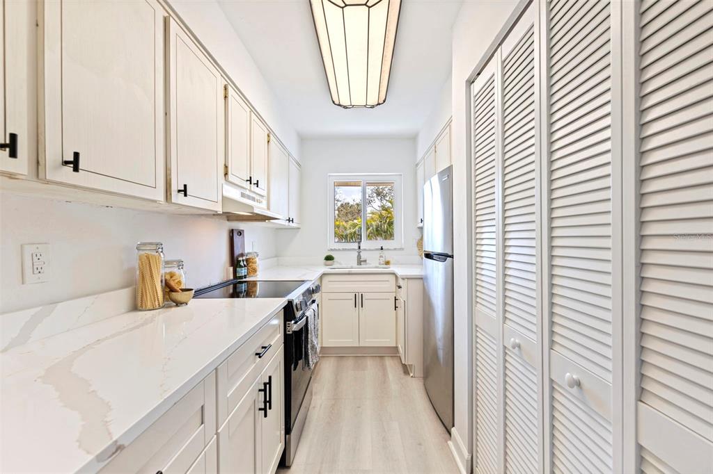 A galley kitchen features white cabinetry, quartz countertops, stainless steel appliances, and louvered closet doors — 4480 OVERLOOK DRIVE NE UNIT 12, ST PETERSBURG, FL