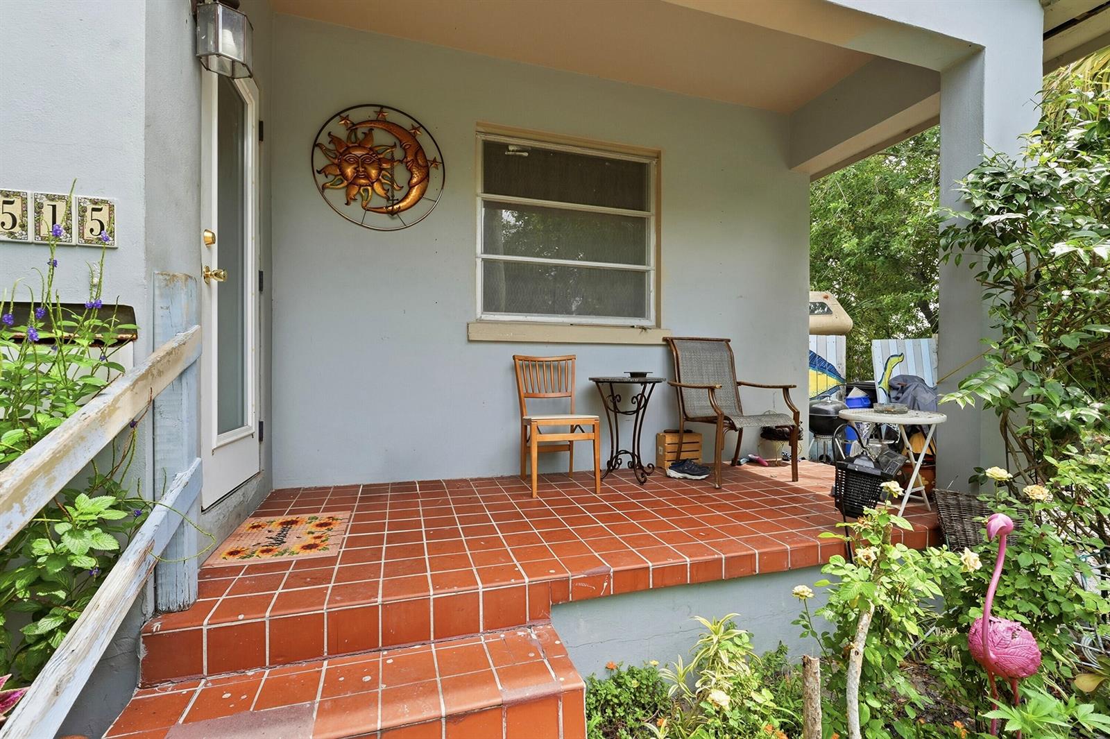 A covered front porch features red tile flooring, two chairs, a small table, and decor — 515 Biscayne Drive, West Palm Beach FL 33401, WEST PALM BEACH, FL