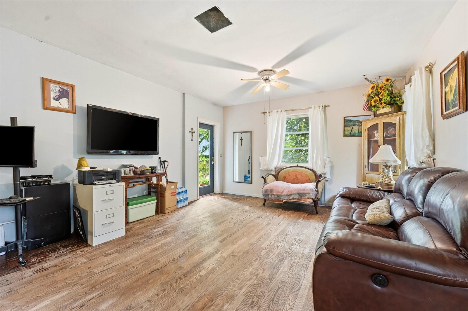 A living room features a brown leather sofa, wood-look flooring, and a wall-mounted television — 515 Biscayne Drive, West Palm Beach FL 33401, WEST PALM BEACH, FL
