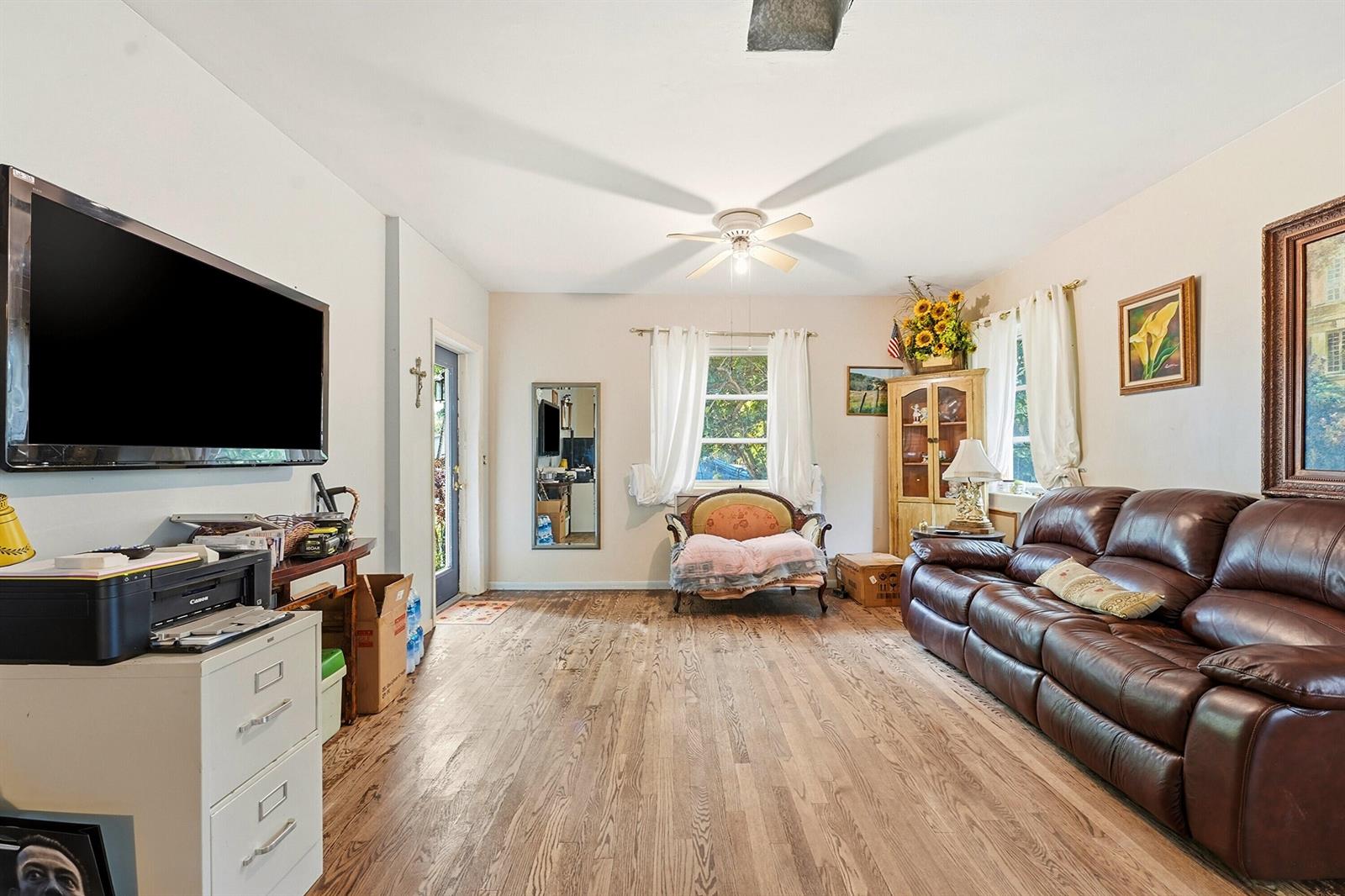 A living room with hardwood floors, a brown leather sofa, a television, and a ceiling fan — 515 Biscayne Drive, West Palm Beach FL 33401, WEST PALM BEACH, FL