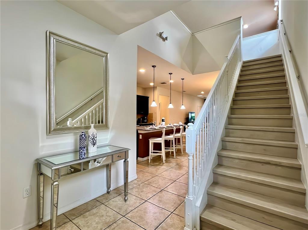 A foyer features a mirrored console table, a wall mirror, and stairs leading to an upper level — 2112 MOROCCO WAY, KISSIMMEE, FL
