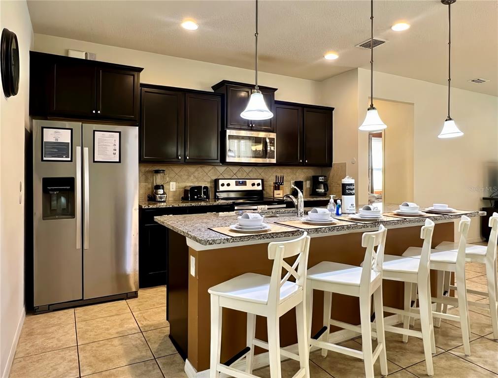 A kitchen features dark wood cabinets, stainless steel appliances, granite countertops, and a breakfast bar — 2112 MOROCCO WAY, KISSIMMEE, FL