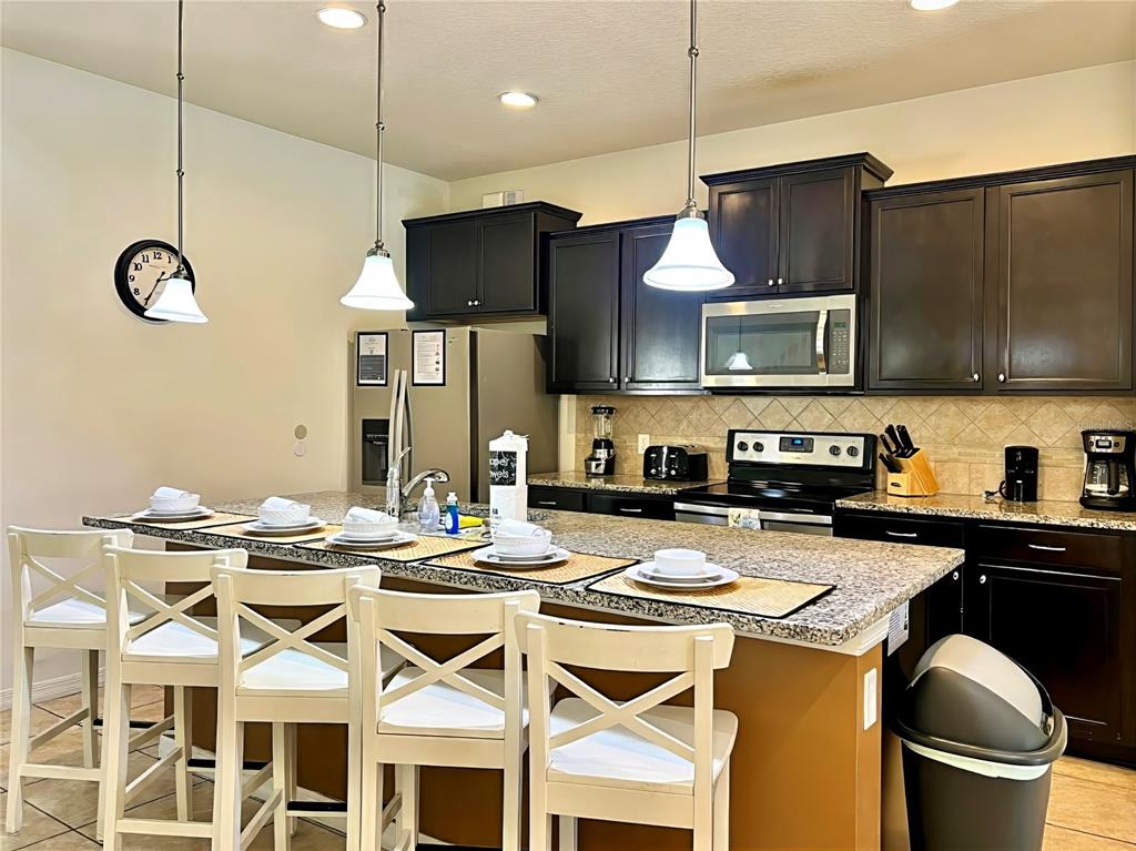 A kitchen features dark cabinetry, granite countertops, a central island with seating, and pendant lighting — 2112 MOROCCO WAY, KISSIMMEE, FL