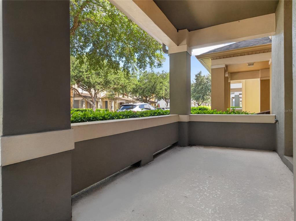 A covered concrete patio features gray walls, thick support columns, and a view of trees — 7735 FAIRGROVE AVENUE, WINDERMERE, FL