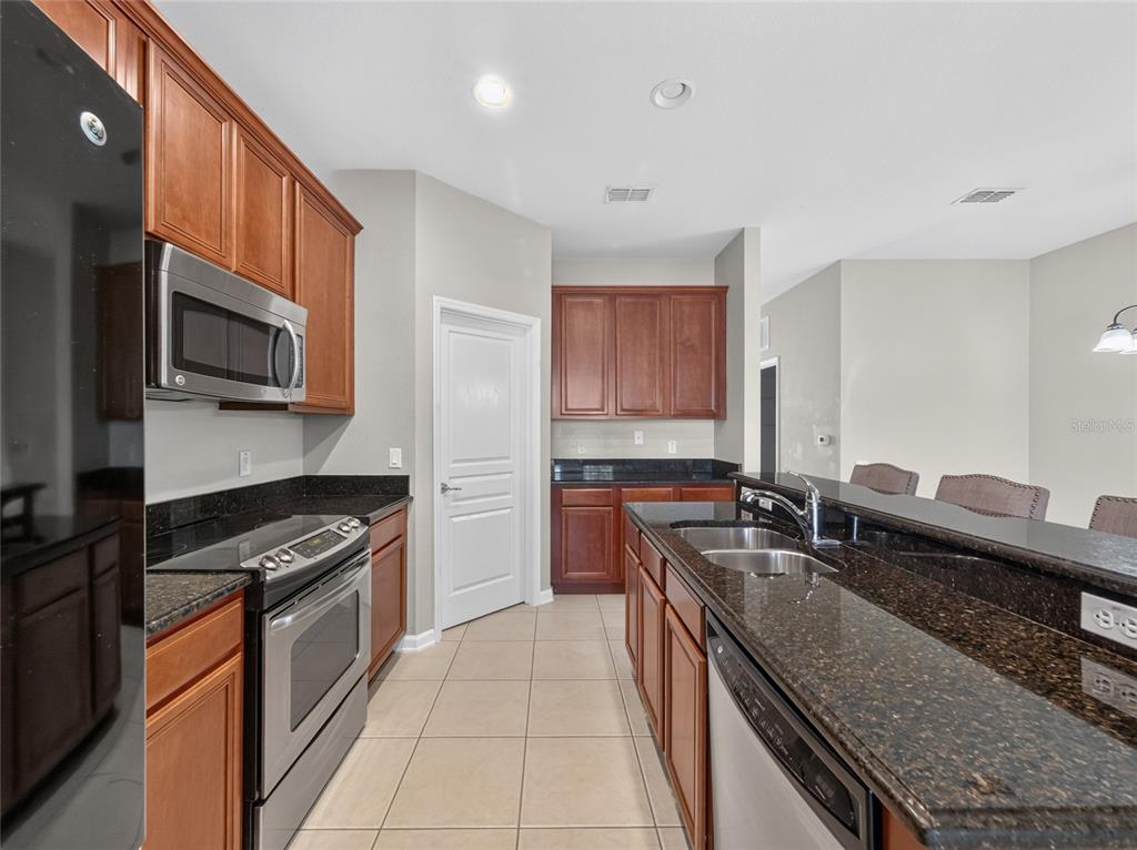A kitchen features wood cabinets, dark granite countertops, stainless steel appliances, and tile flooring — 7735 FAIRGROVE AVENUE, WINDERMERE, FL