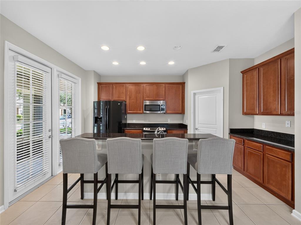 A kitchen features wooden cabinets, black countertops, a breakfast bar with four chairs, and tile flooring — 7735 FAIRGROVE AVENUE, WINDERMERE, FL