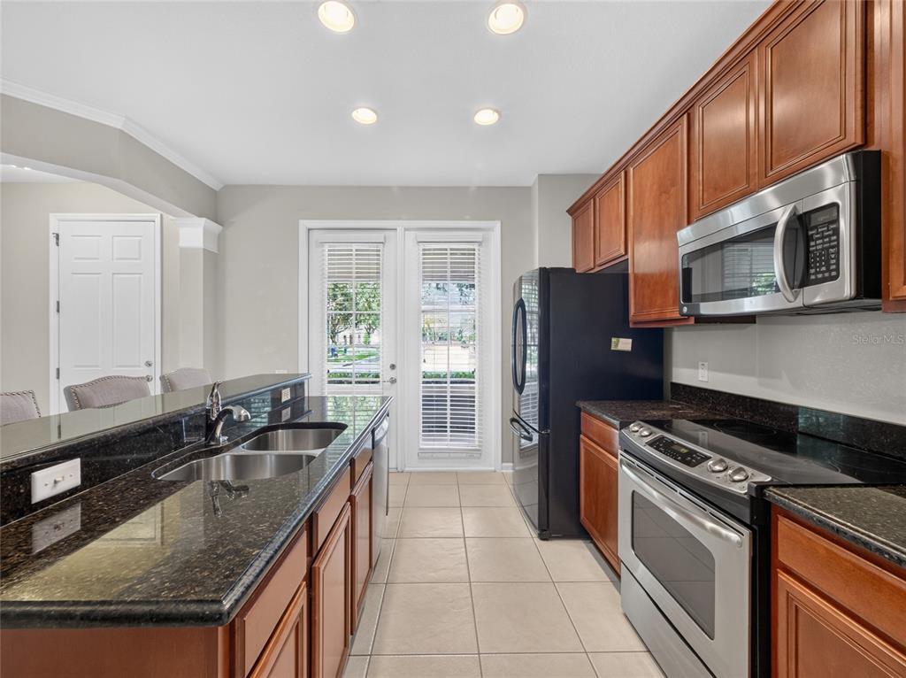 A kitchen features dark granite countertops, wood cabinets, stainless steel appliances, and tile flooring — 7735 FAIRGROVE AVENUE, WINDERMERE, FL