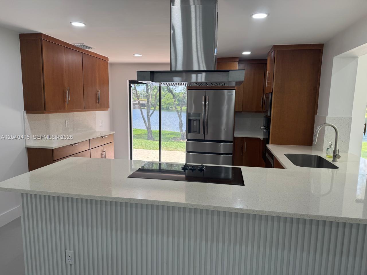 A kitchen features wood cabinets, white countertops, a center island with a cooktop, and water views — 2360 Dover, Weston FL 33326, WESTON, FL