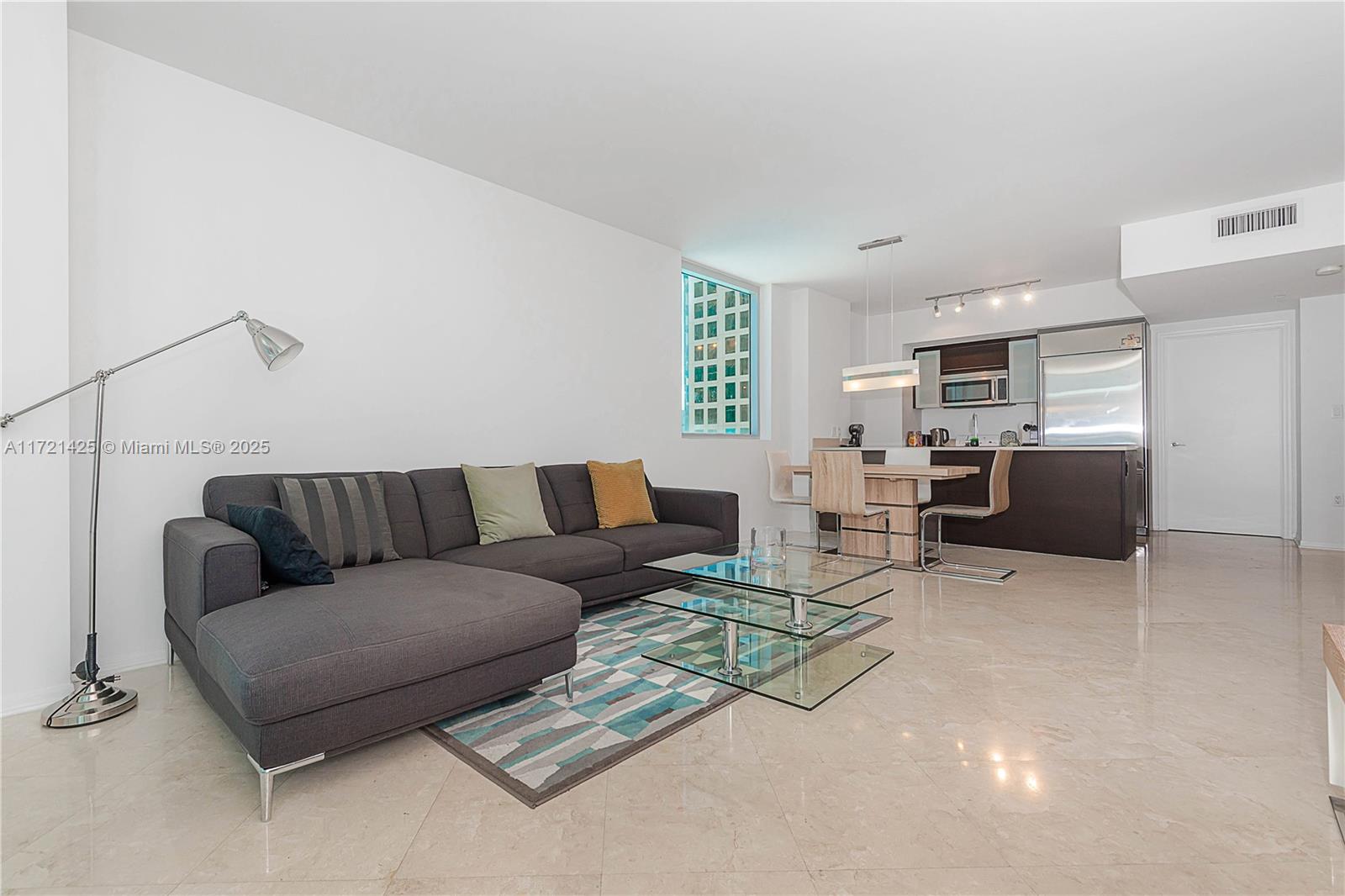 A living room with a grey sectional sofa, glass coffee table, and an open kitchen — 55 SE 6th St # 1507, Miami FL 33131, MIAMI, FL