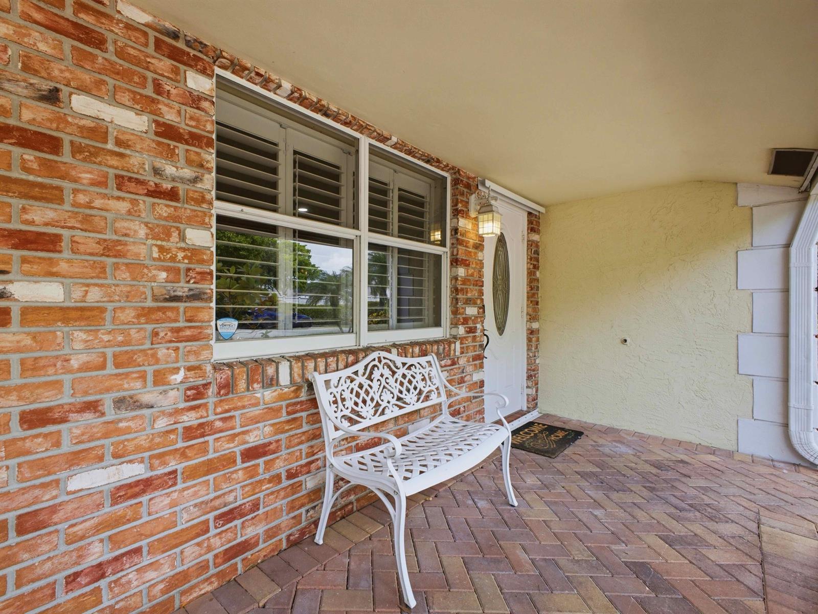 A white metal bench sits on a brick-paved porch in front of a brick house — 5120 NE 22nd Avenue, Lighthouse Point FL 33064, LIGHTHOUSE POINT, FL