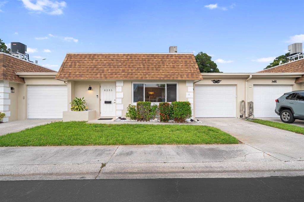A single-story townhouse with a brown shingled roof, white garage doors, and a front lawn — 8235 BURGUNDY DRIVE N UNIT 3, PINELLAS PARK, FL