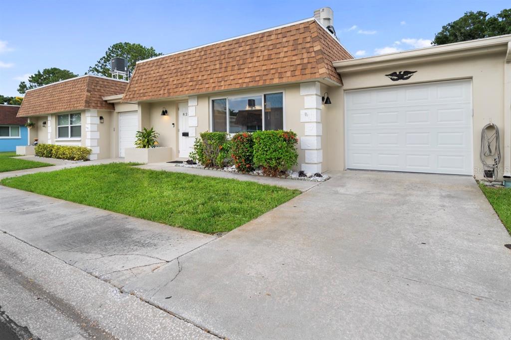 A single-story house with a brown shingled mansard roof, white garage door, and front lawn — 8235 BURGUNDY DRIVE N UNIT 3, PINELLAS PARK, FL