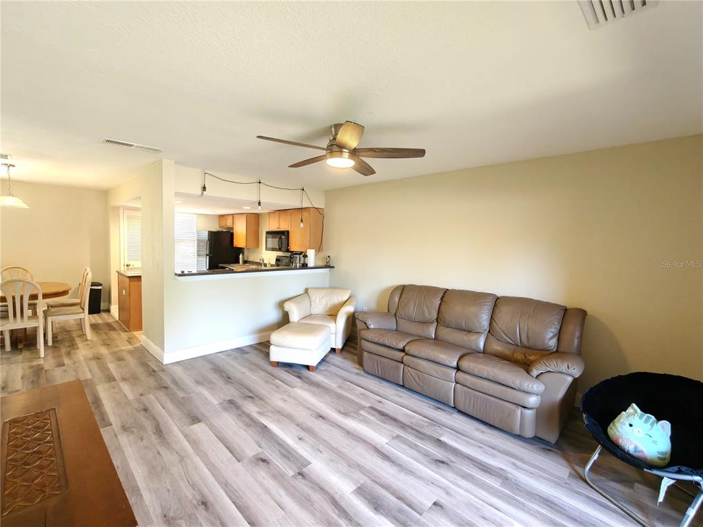 A living room with wood-look flooring, a leather sofa, and an open kitchen area — 1810 NW 23RD BOULEVARD UNIT 165, GAINESVILLE, FL