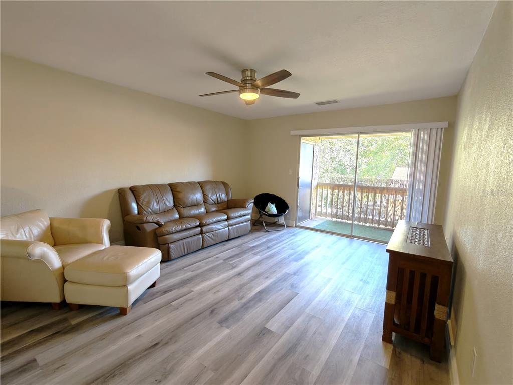 A living room features light wood-look flooring, a ceiling fan, leather seating, and a sliding door — 1810 NW 23RD BOULEVARD UNIT 165, GAINESVILLE, FL