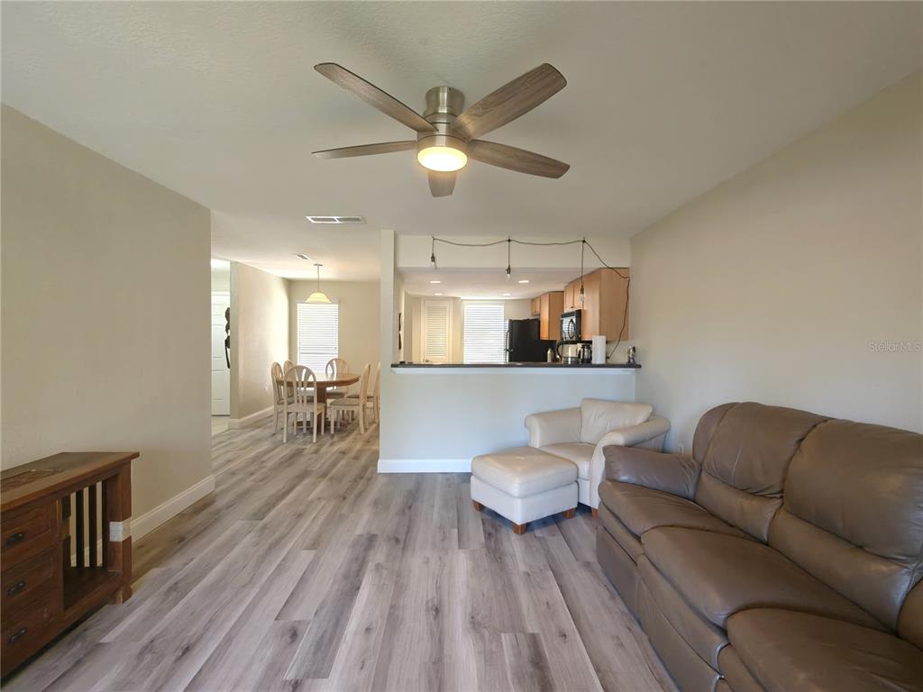 A living room with wood-look flooring, a ceiling fan, and an open kitchen view — 1810 NW 23RD BOULEVARD UNIT 165, GAINESVILLE, FL