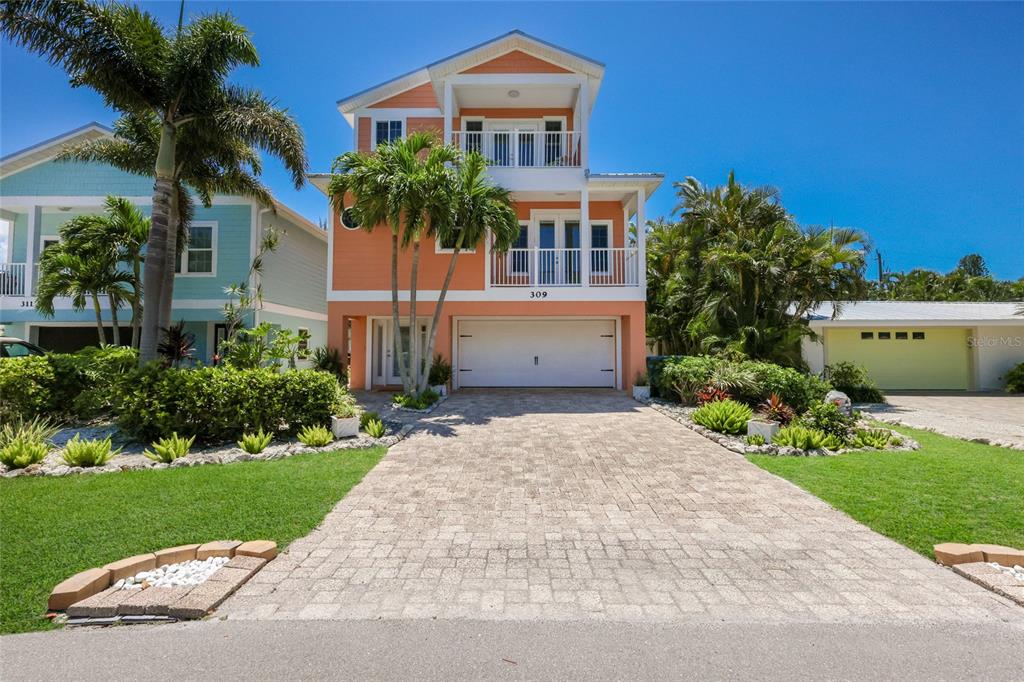 A three-story orange house with a paved driveway and palm trees under a clear sky — 309 68TH STREET, HOLMES BEACH, FL
