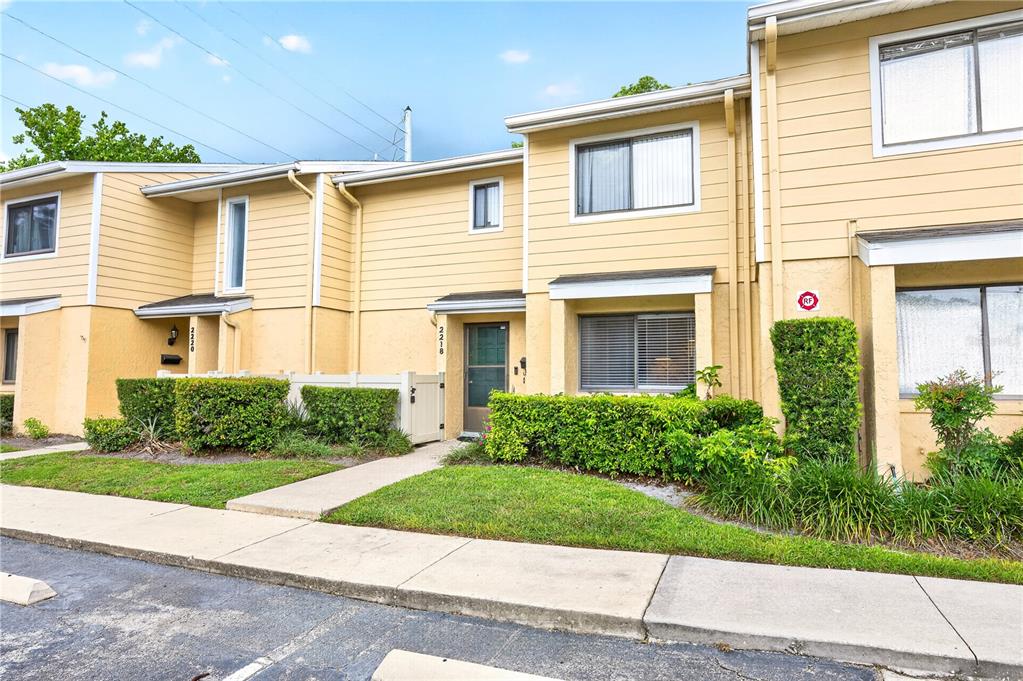 The exterior of a two-story townhouse complex features yellow siding, green hedges, and concrete walkways — 2218 MCMAHON COURT UNIT 1038, ORLANDO, FL
