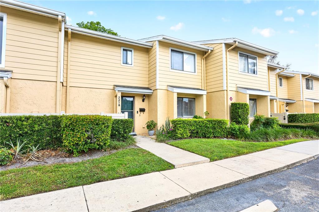 A two-story yellow townhouse with a front walkway and manicured hedges — 2218 MCMAHON COURT UNIT 1038, ORLANDO, FL