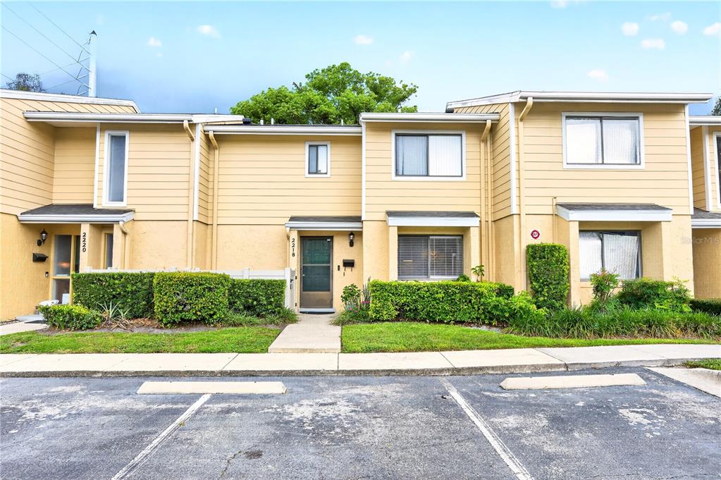 A row of two-story townhouses with yellow siding, green hedges, and a parking lot — 2218 MCMAHON COURT UNIT 1038, ORLANDO, FL