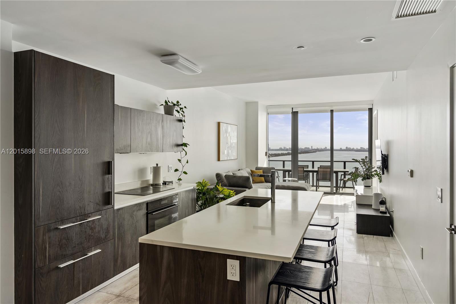 A modern kitchen with dark wood cabinetry and a white island overlooks a balcony view — 480 NE 31st St # 1802, Miami FL 33137, MIAMI, FL