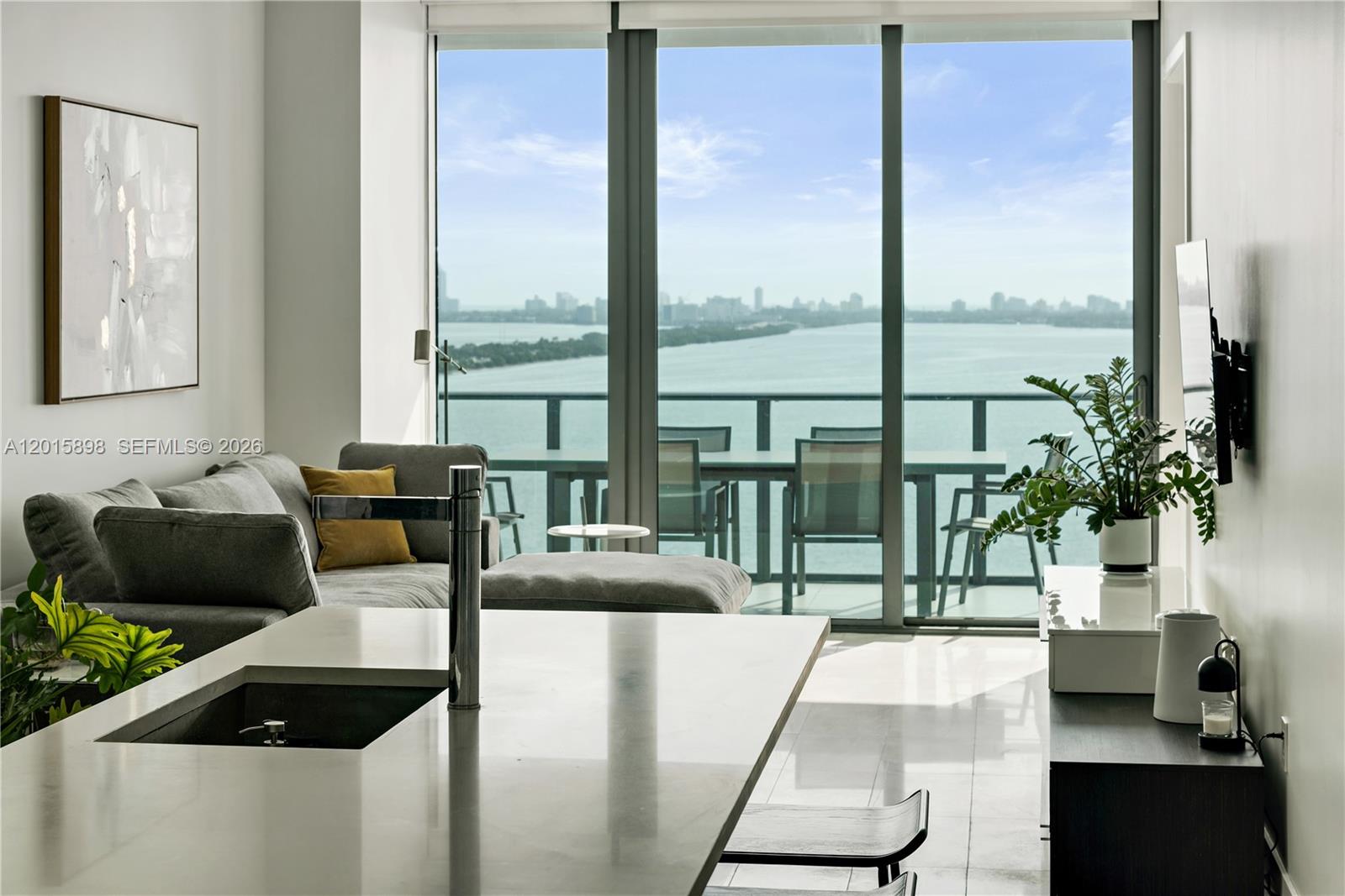A modern kitchen island overlooks a living area with floor-to-ceiling windows and a water view — 480 NE 31st St # 1802, Miami FL 33137, MIAMI, FL