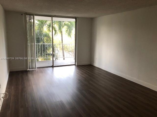 An empty room with dark wood-look flooring and a sliding glass door leading to a balcony — 498 NW 165th St Rd # 304, Miami FL 33169, MIAMI, FL