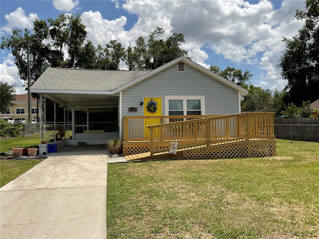 A light blue house features a yellow front door and a wooden wheelchair access ramp — 37204 MAGNOLIA AVENUE, DADE CITY, FL