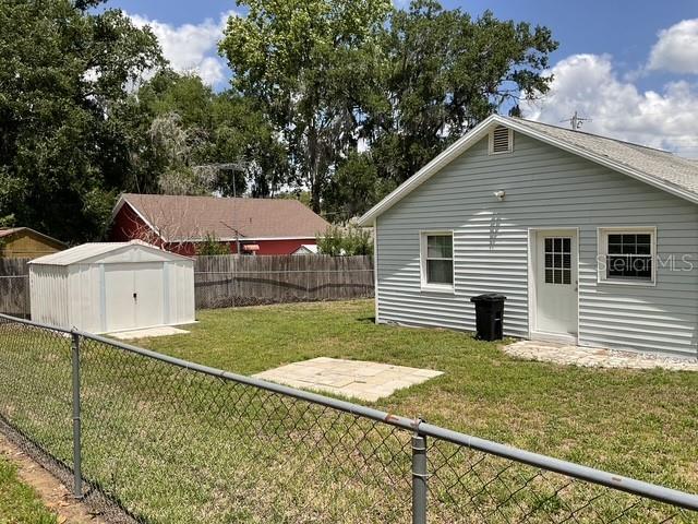 A backyard features a white metal shed, a light-colored house, and a chain-link fence — 37204 MAGNOLIA AVENUE, DADE CITY, FL