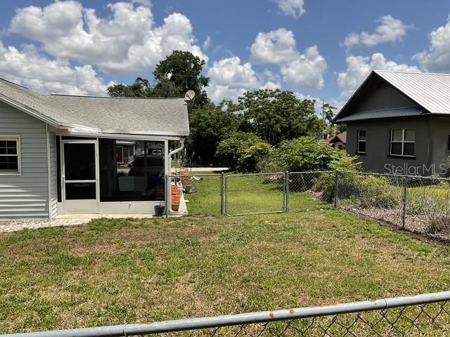 A view of a backyard with a chain-link fence, a screened porch, and neighboring houses — 37204 MAGNOLIA AVENUE, DADE CITY, FL