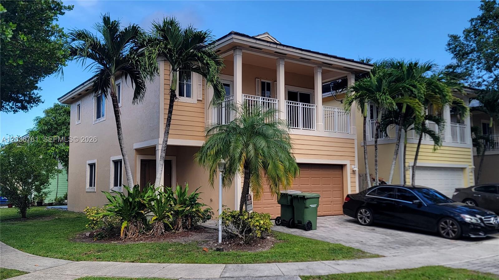 A two-story tan house with a garage, balcony, and palm trees in the front yard — 391 NE 33rd Ter, Homestead FL 33033, HOMESTEAD, FL
