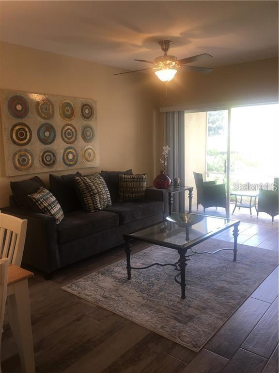 A living room features a dark sofa, a glass coffee table, and a ceiling fan — 1231 GODAVARI WAY UNIT 103, WESLEY CHAPEL, FL