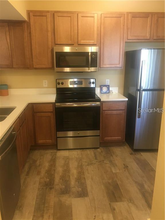 A kitchen features wood cabinets, stainless steel appliances, white countertops, and wood-look tile flooring — 1231 GODAVARI WAY UNIT 103, WESLEY CHAPEL, FL