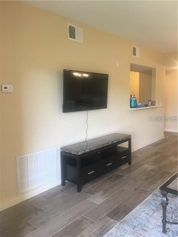 A living room features a wall-mounted television, a media console, and light-colored tile flooring — 1231 GODAVARI WAY UNIT 103, WESLEY CHAPEL, FL