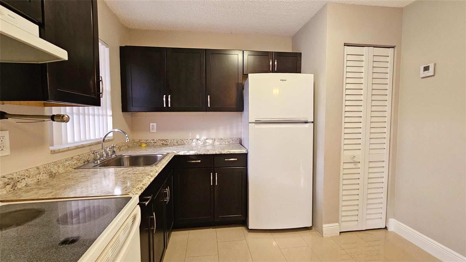 A kitchen features dark wood cabinets, granite countertops, a white refrigerator, and tile flooring — 416 Lakeside Drive # 129, Margate FL 33063, MARGATE, FL