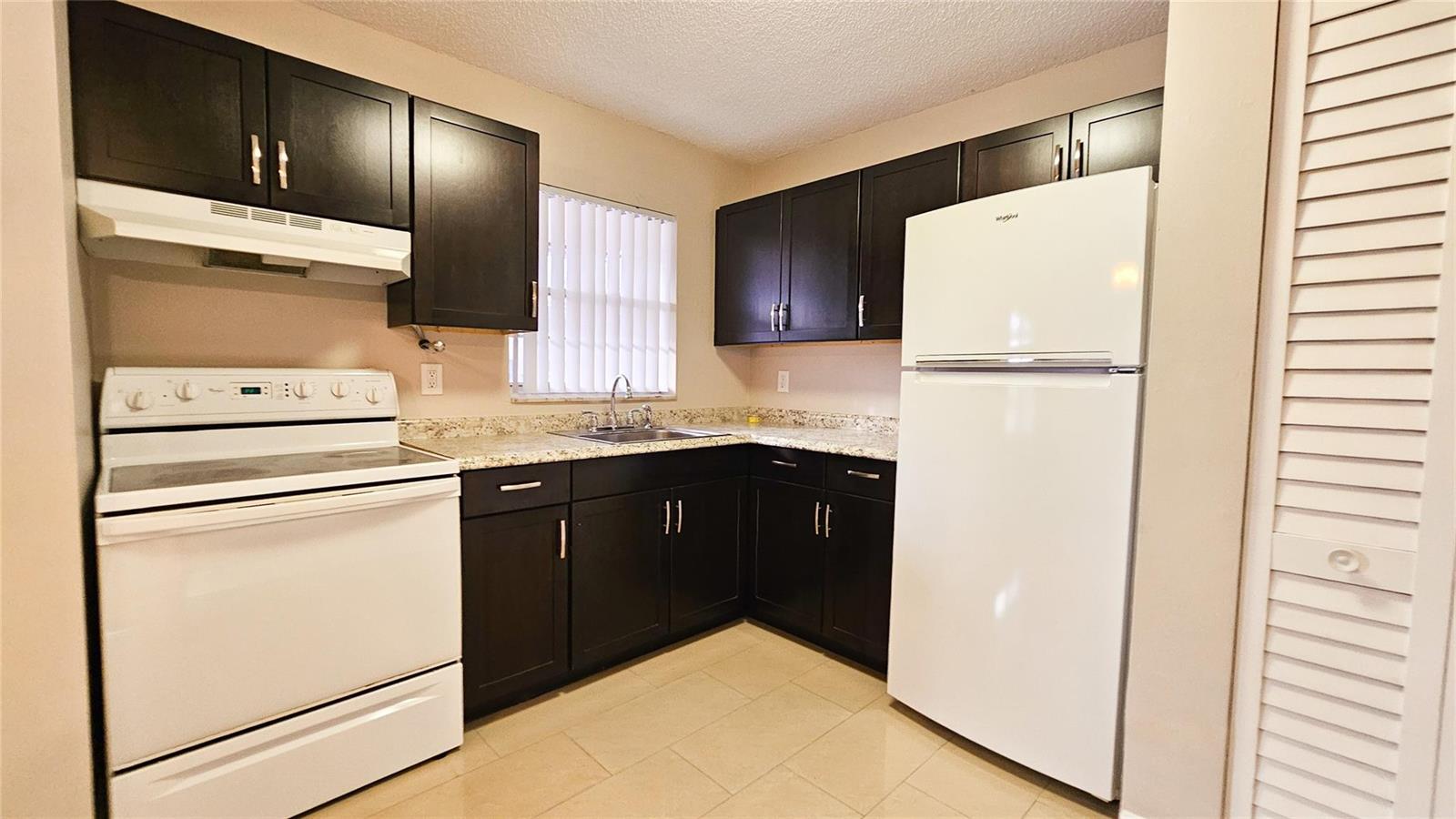 A kitchen features dark wood cabinets, white appliances, and light-colored countertops — 416 Lakeside Drive # 129, Margate FL 33063, MARGATE, FL