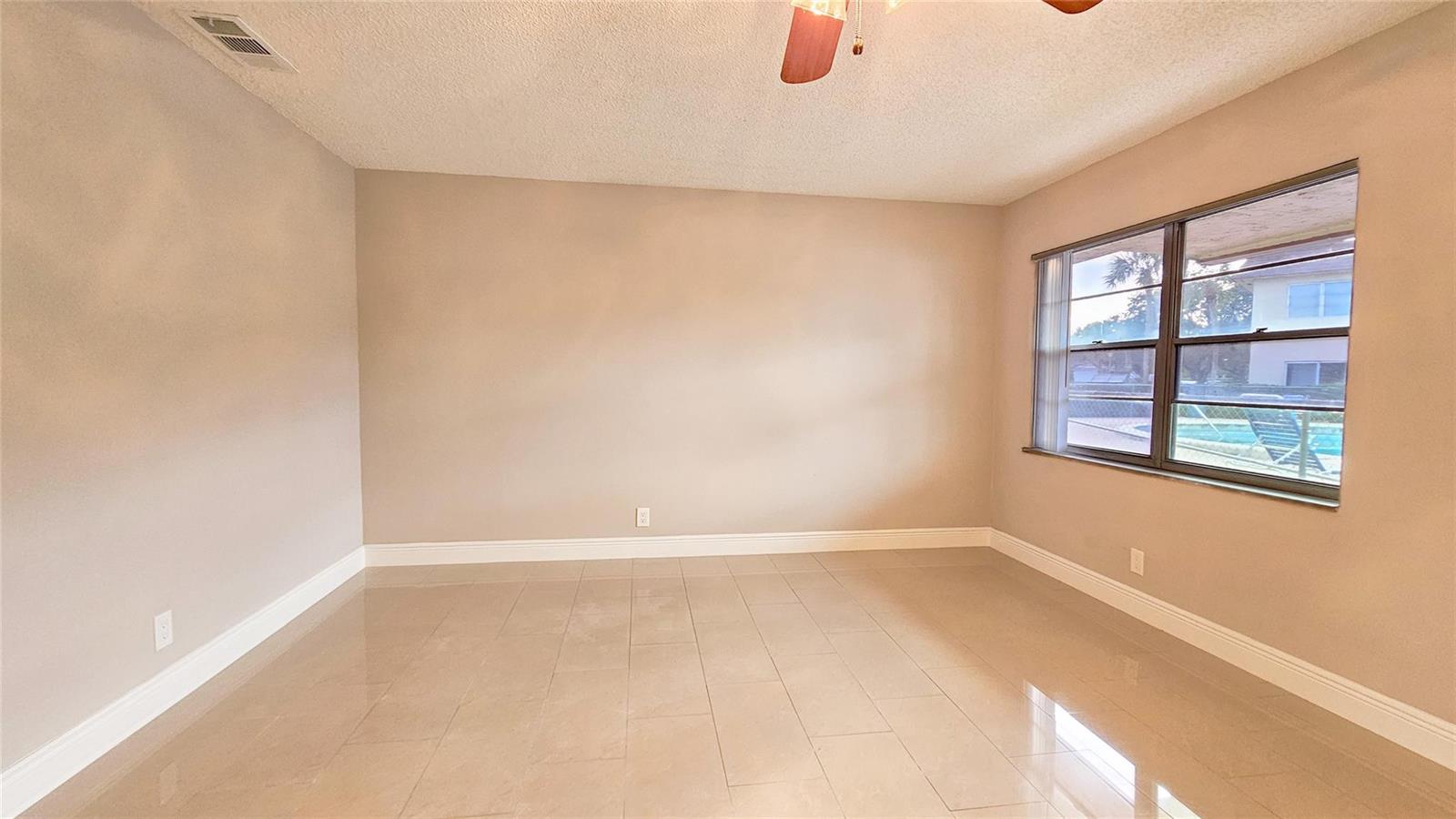 An empty room with beige walls, light-colored tile flooring, and a window overlooking a pool — 416 Lakeside Drive # 129, Margate FL 33063, MARGATE, FL