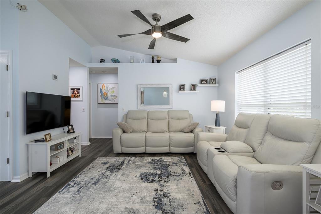 A living room features a white sofa, a reclining loveseat, a television, and dark flooring — 6 SPIVEYS COURT, ORMOND BEACH, FL