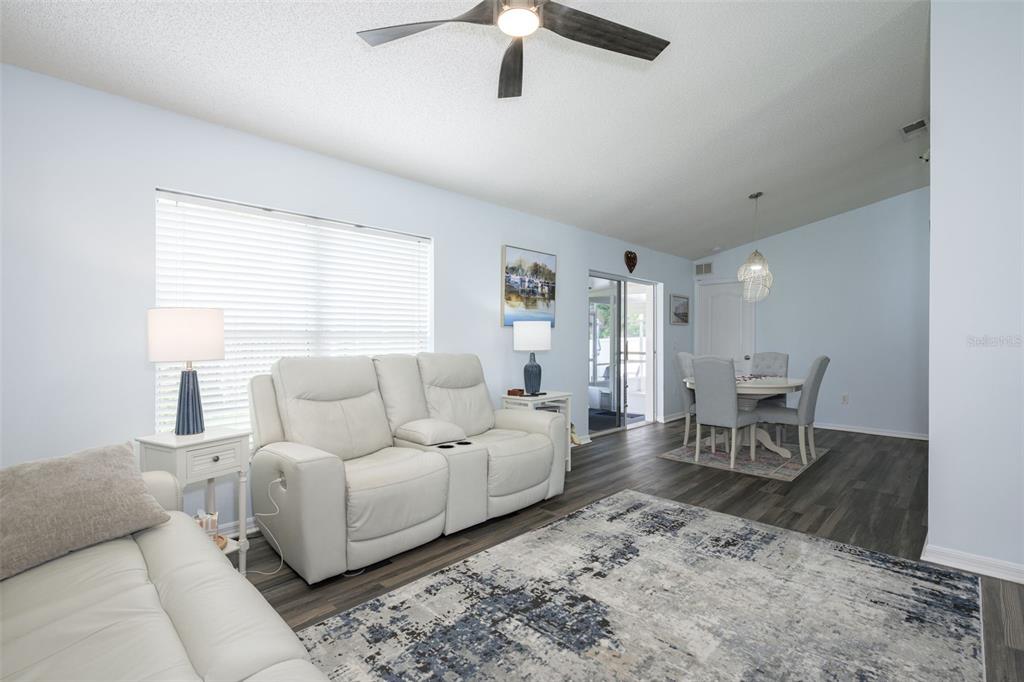 A living room with light blue walls, white leather sofas, and dark wood-look flooring — 6 SPIVEYS COURT, ORMOND BEACH, FL