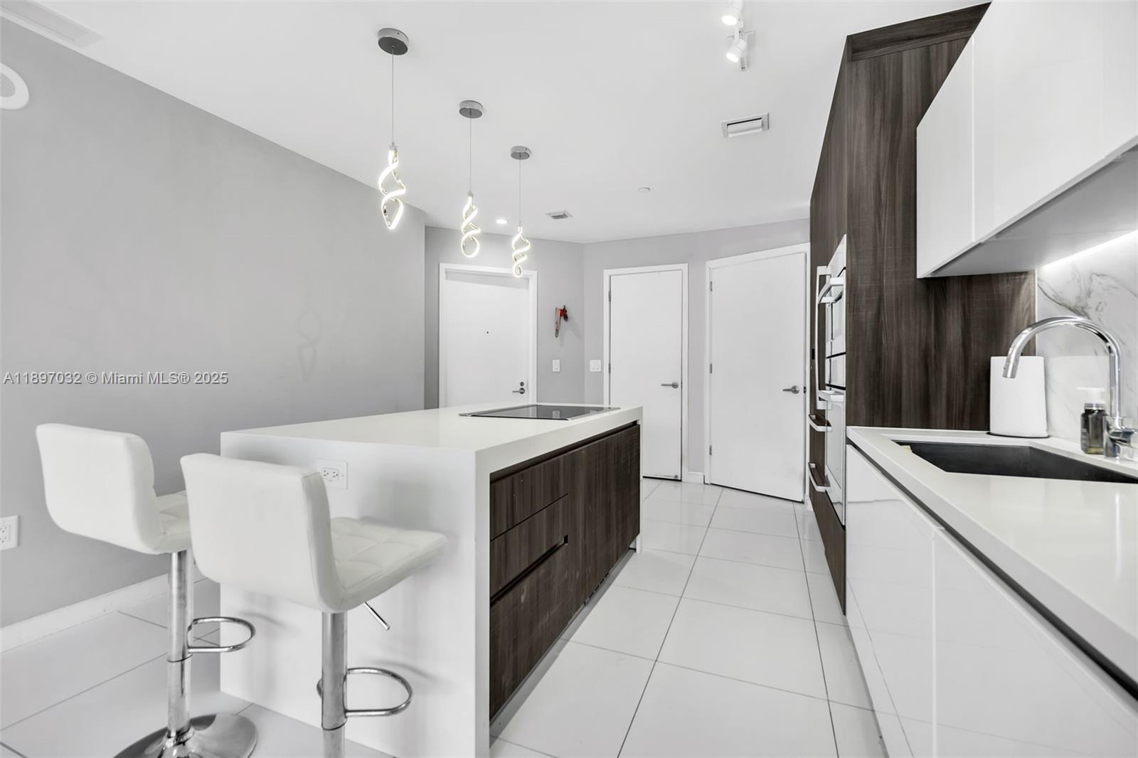 A modern kitchen features a white island with a cooktop, bar stools, and dark cabinetry — 851 NE 1st Ave # 806, Miami FL 33132, MIAMI, FL