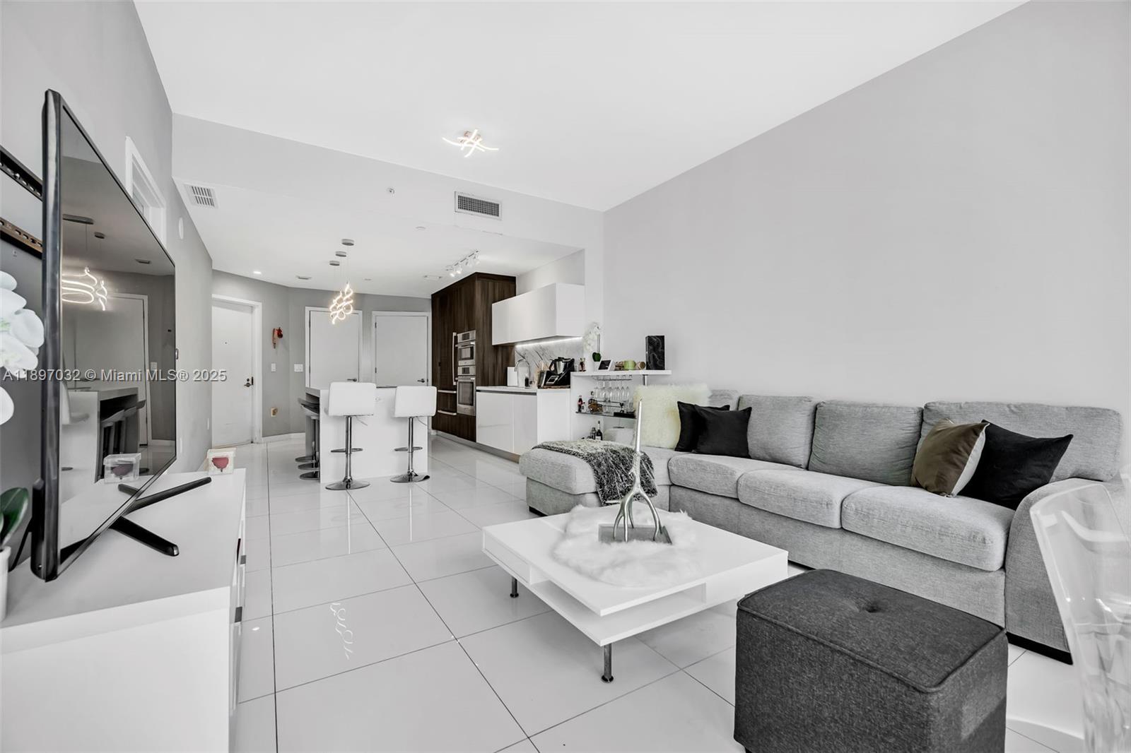 A modern living room features a grey sectional sofa, white coffee table, and open kitchen — 851 NE 1st Ave # 806, Miami FL 33132, MIAMI, FL
