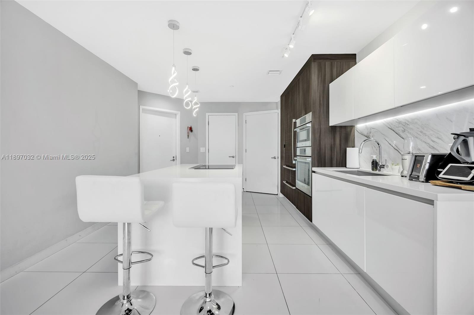 A modern kitchen features white cabinetry, a central island with bar stools, and stainless appliances — 851 NE 1st Ave # 806, Miami FL 33132, MIAMI, FL