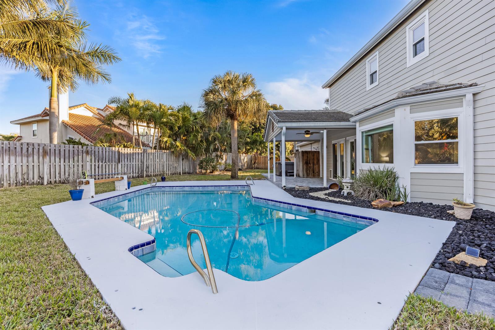 A backyard features a rectangular swimming pool, a covered patio, and a two-story house exterior — INDIALANTIC, FL