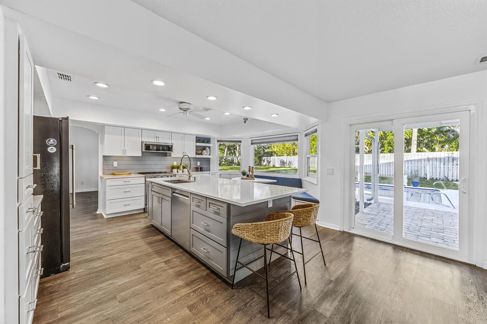 A modern kitchen features a gray island, white cabinetry, wood-look flooring, and sliding glass patio doors — INDIALANTIC, FL