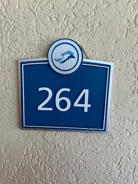 A blue room number sign labeled 264 is mounted on a textured beige wall — 102 YACHT HARBOR DRIVE UNIT 264, PALM COAST, FL