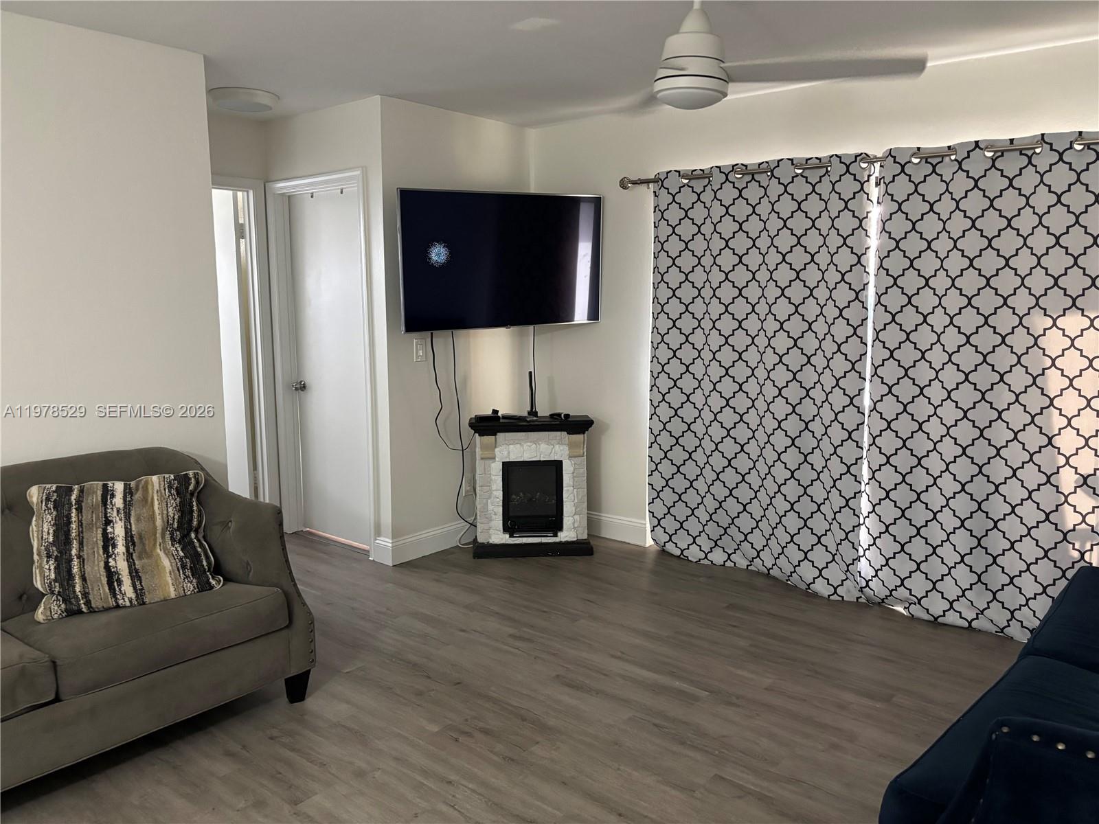 A living room features a wall-mounted television above a small electric fireplace and patterned curtains — 3615 NW 94th Ave # 8F, Sunrise FL 33351, SUNRISE, FL