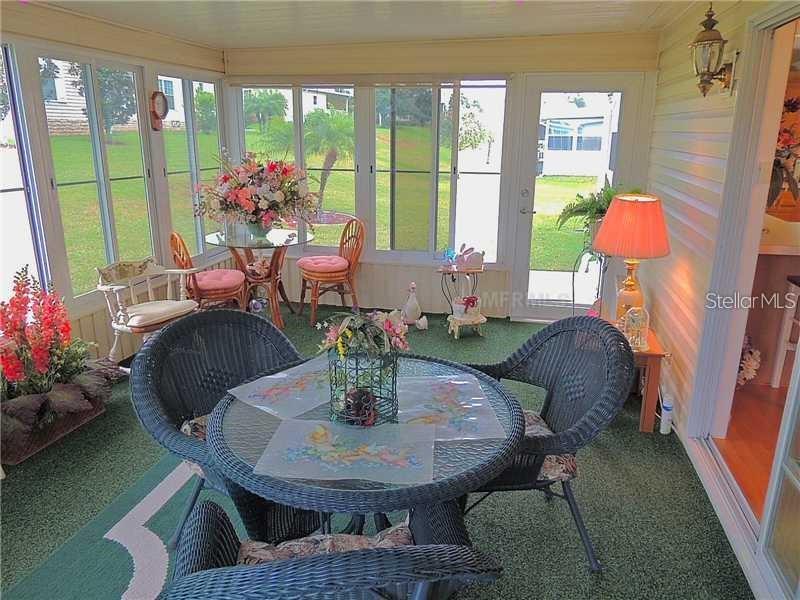 A sunroom features wicker furniture, a glass-topped table, green carpeting, and large windows overlooking grass — 37535 NEW HORIZONS BOULEVARD, ZEPHYRHILLS, FL